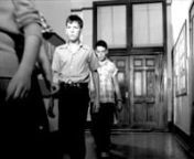 Post-structuralist study. School children emerge slowly from a classroom during an air raid preparedness drill - circa early 1950s - demonstrating a culture that fosters fear, alarm, sadness, trauma, and a frightening level of conformity.nnThere is a strong level of awareness and performativity in the facial expressions of the children. They are well aware that a camera is recording them, yet their faces betray a wide array of strong emotions; from anger to boredom to fear. The children behave a